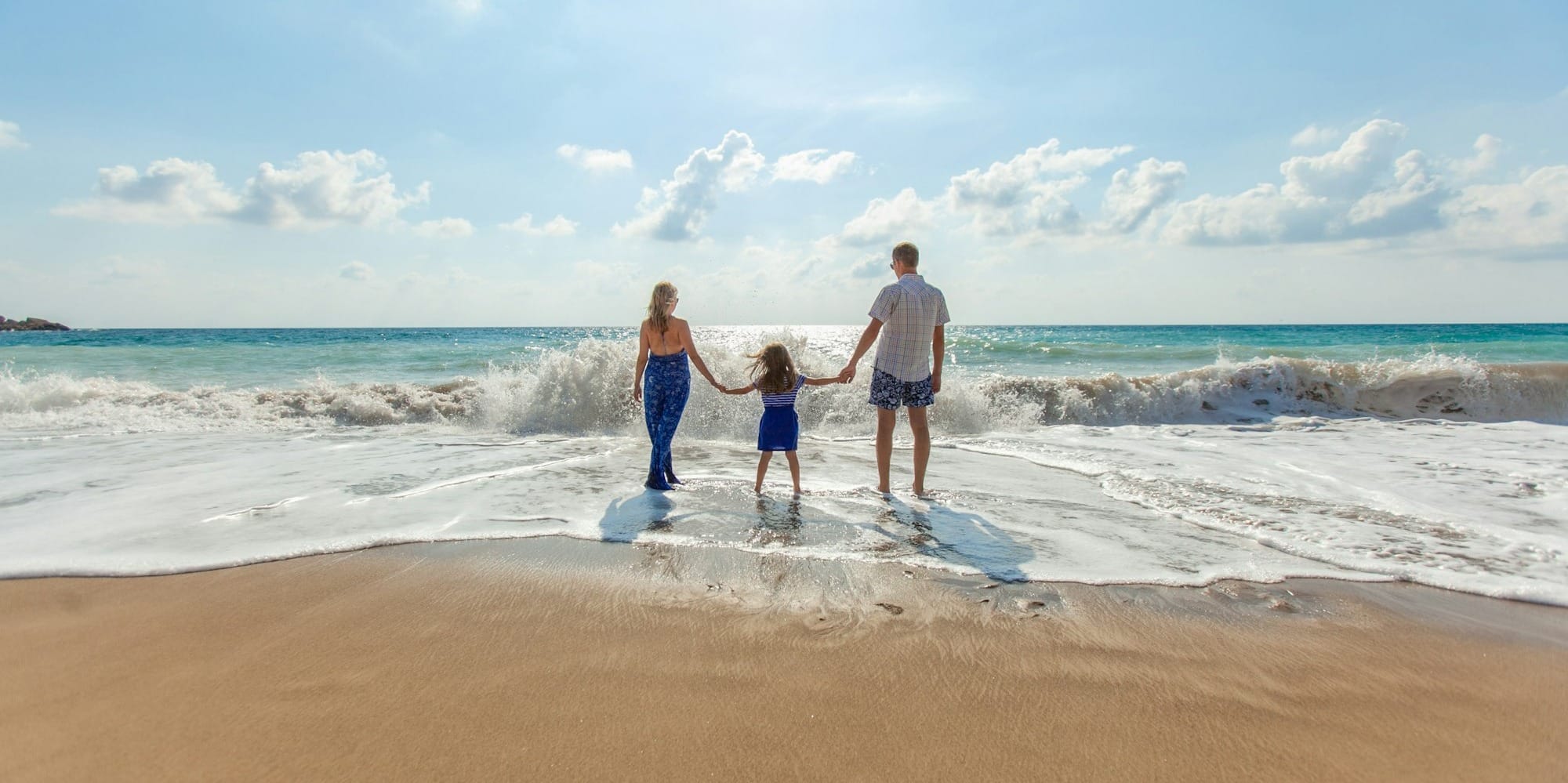 man, woman and child holding hands on seashore