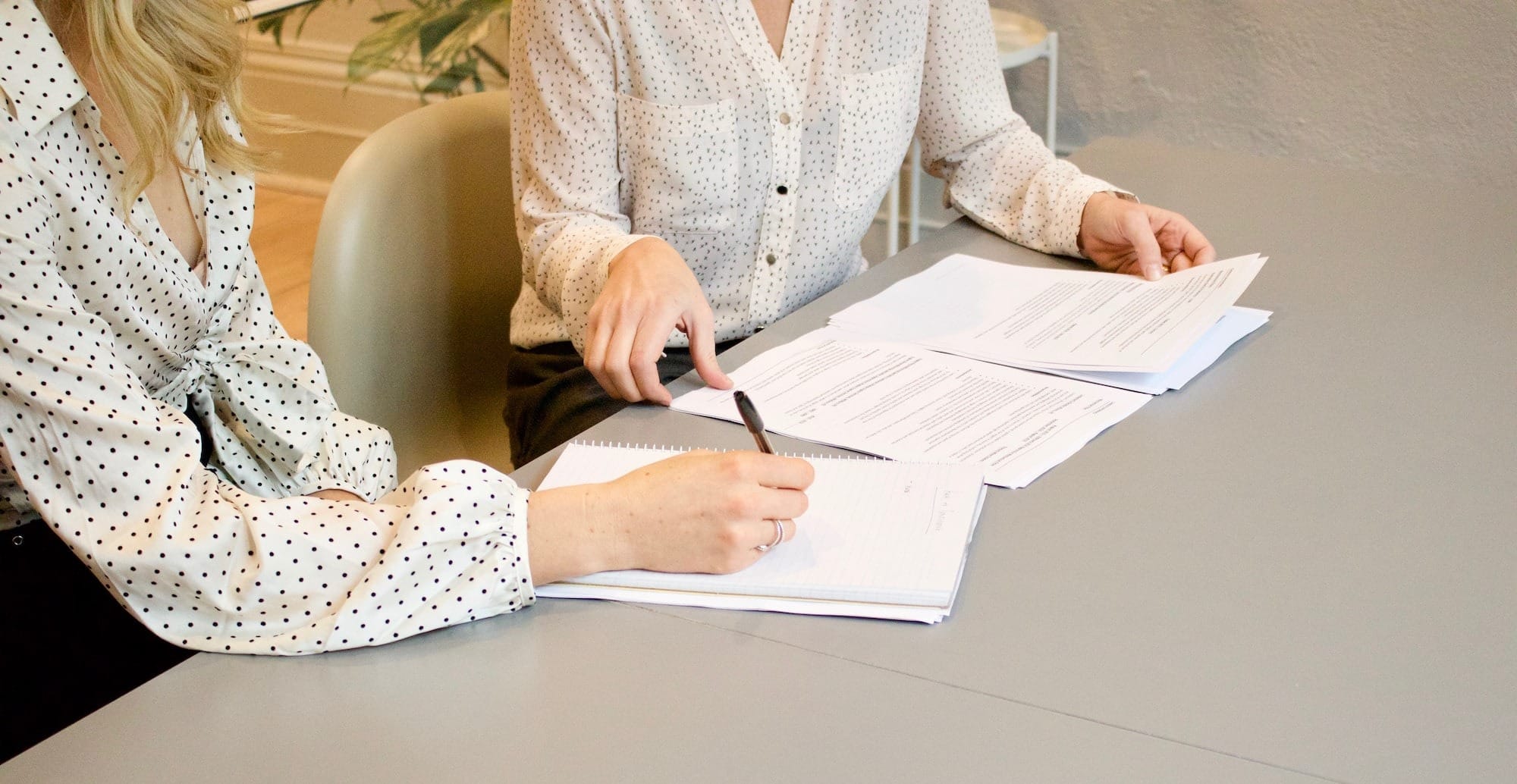 woman signing on white printer paper beside woman about to touch the documents